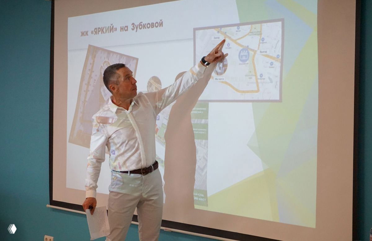 Мужчина в белой рубашке стоит у экрана и указывает на слайд с картой и схемами — кадр с презентации проектных решений в строительстве.
