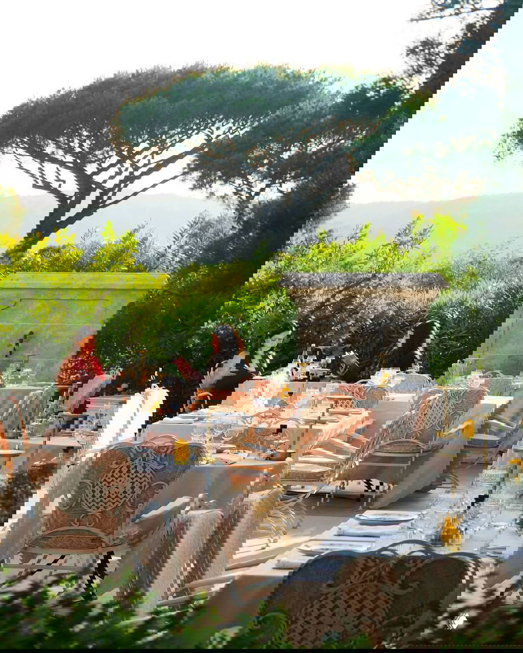 Терасса ресторана отеля с сервированными столиками на открытом воздухе, двумя посетительницами и типичным средиземноморским видом вокруг.