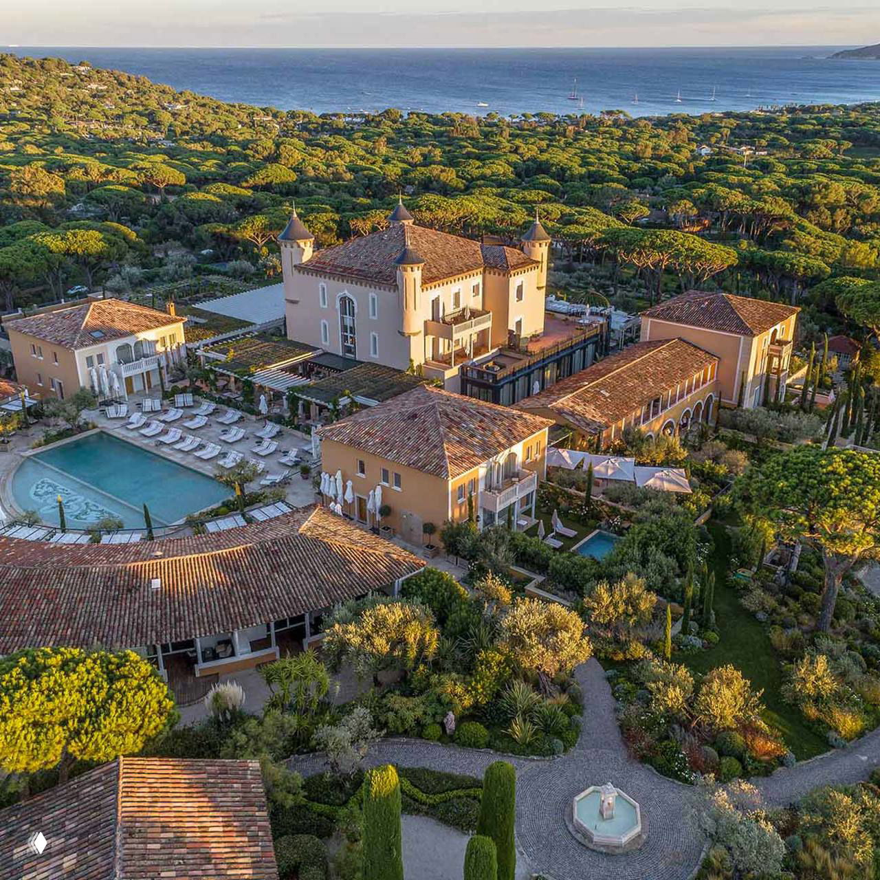 Панорамный кадр комплекса отеля у моря: крыши, открытые бассейны, извилистые дорожки и сосновые насаждения на Лазурном берегу рядом с заливом.