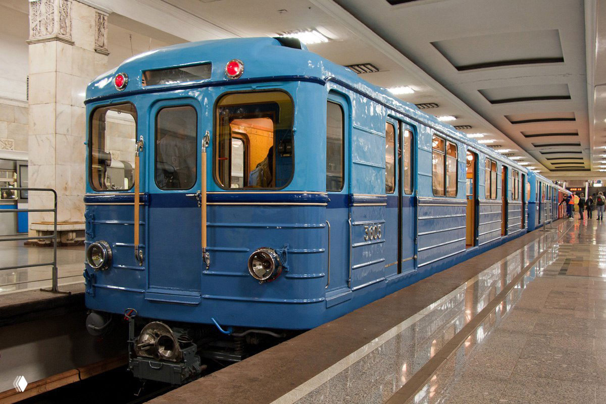 Синий ретровагон на платформе метро: металлический корпус, круглые фары, мраморная платформа и пассажиры в глубине станции