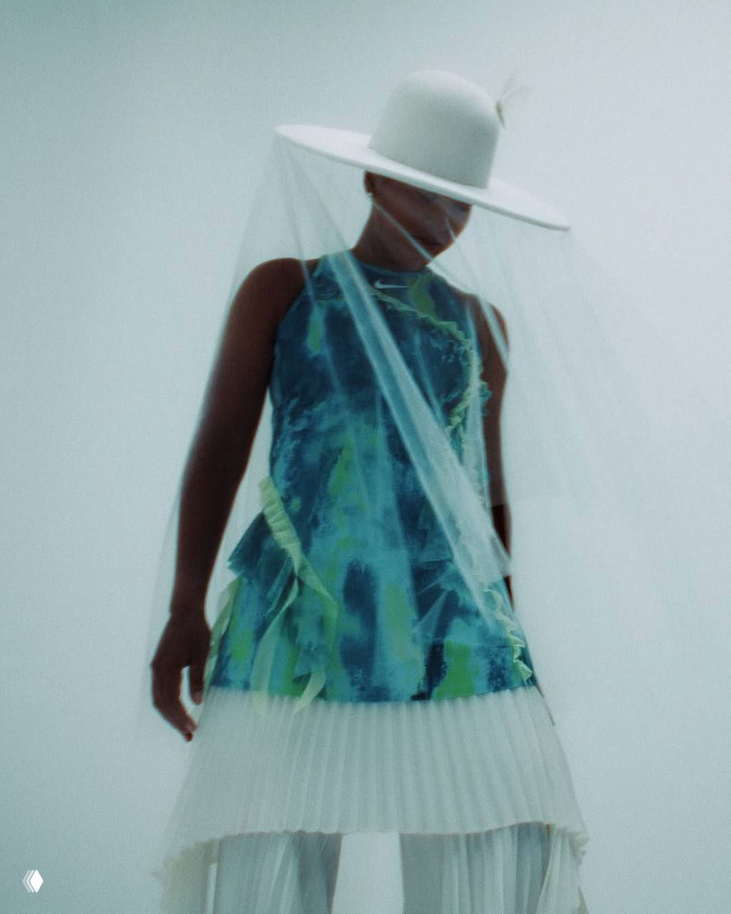 Модель в длинном платье с абстрактным принтом и шляпой с вуалью: лёгкая размытость кадра подчёркивает художественную подачу образа.