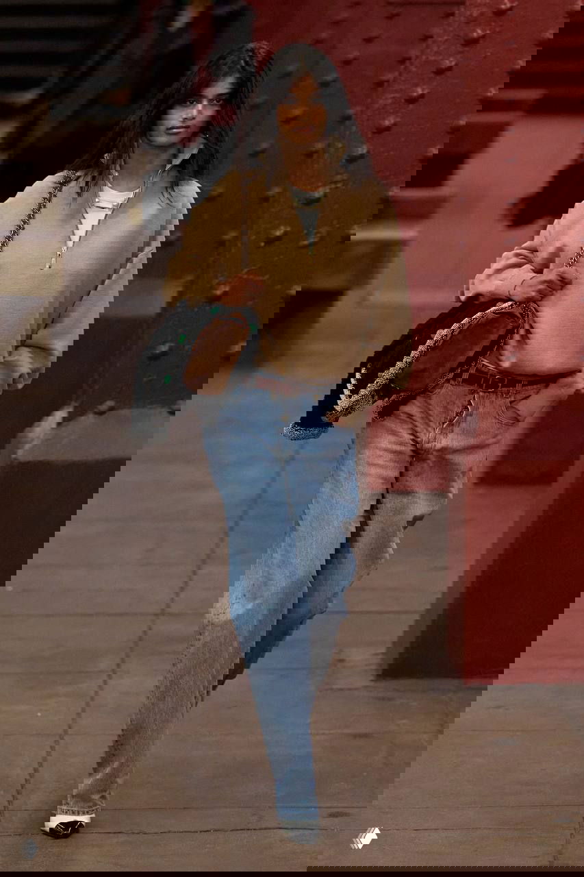 Модель в бежевом свитшоте, широких светлых джинсах и туфлях с контрастным мысом идет по платформе нью-йоркской станции метро во время шоу Chanel.