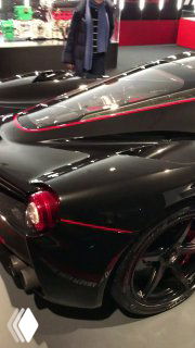 Чёрная спортивная Ferrari крупным планом: кузов, аэродинамические линии и красные акценты на корпусе в выставочном зале.