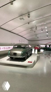 Часть экспозиции Ferrari в музее: ракурс на заднюю часть редкой модели на подиуме в минималистичном белом зале музея.