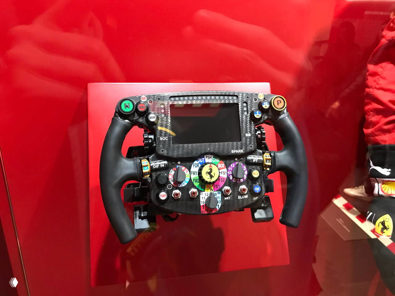 Рулевое колесо болида Ferrari в витрине: множество переключателей и индикаторов, демонстрация технологичности органов управления в гонках.