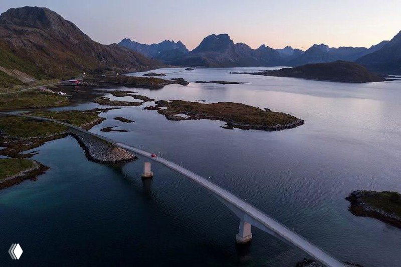 Панорамный вид на мост через фьорд и мелкие острова, спокойная вода и горы на заднем плане — типичный фьордовый пейзаж Норвегии.