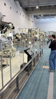 Роботы и фрагмент сборочного конвейера в музее Toyota, посетитель наблюдает автоматизированные линии и элементы промышленной автоматизации.