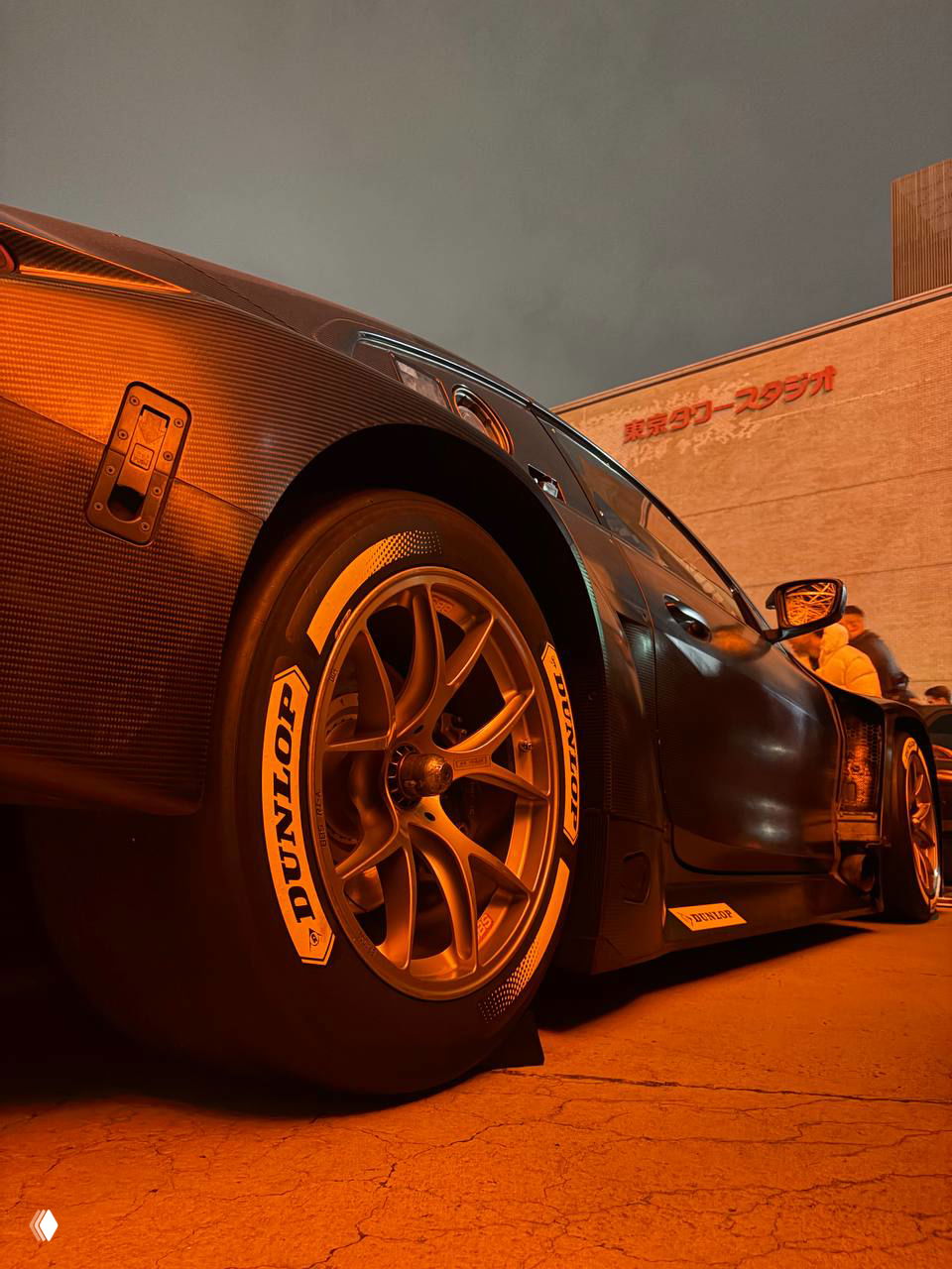 Открытый капот спортивного автомобиля, вид на тюнингованный рядный мотор с турбонагнетателем и серебристые впускные трубы, ночная техника на показе.