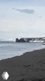 Пустынный берег Камчатки с чёрным вулканическим песком, скалистыми утёсами и серым морем под облачным небом.