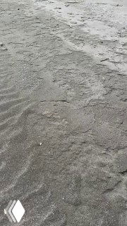 Чёрный вулканический песок вблизи, рисунки от воды и ветра, текстура побережья Камчатки в макро-кадре.