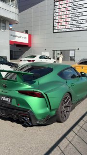 Задняя часть зелёной Toyota Supra TOMS Edition на автодроме с заметным антикрылом, расширителями крыльев и спортивным диффузором.