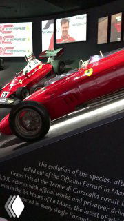 Выставка исторических гонок и экспонатов Ferrari: стенды с информацией и образцы старых гоночных автомобилей и экспонатов.