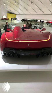 Задняя часть современной модели Ferrari внутри музея, вид на агрессивный диффузор и световую линию заднего фонаря на подиуме.